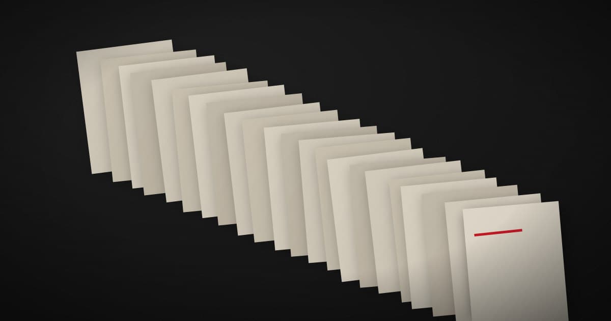 Stacked pale paper sheets on a dark surface, most of them blank, with one page marked by a crimson line