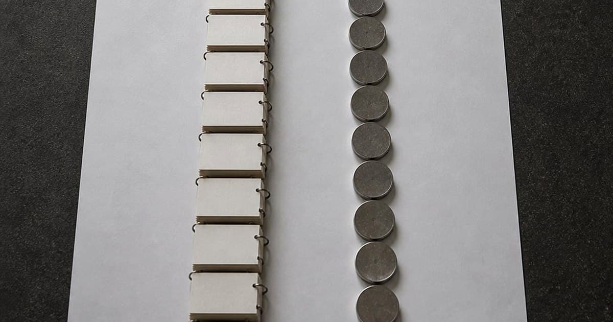 Two parallel columns laid out on paper, one of index cards and one of stacked coins, running from a red-spined ledger