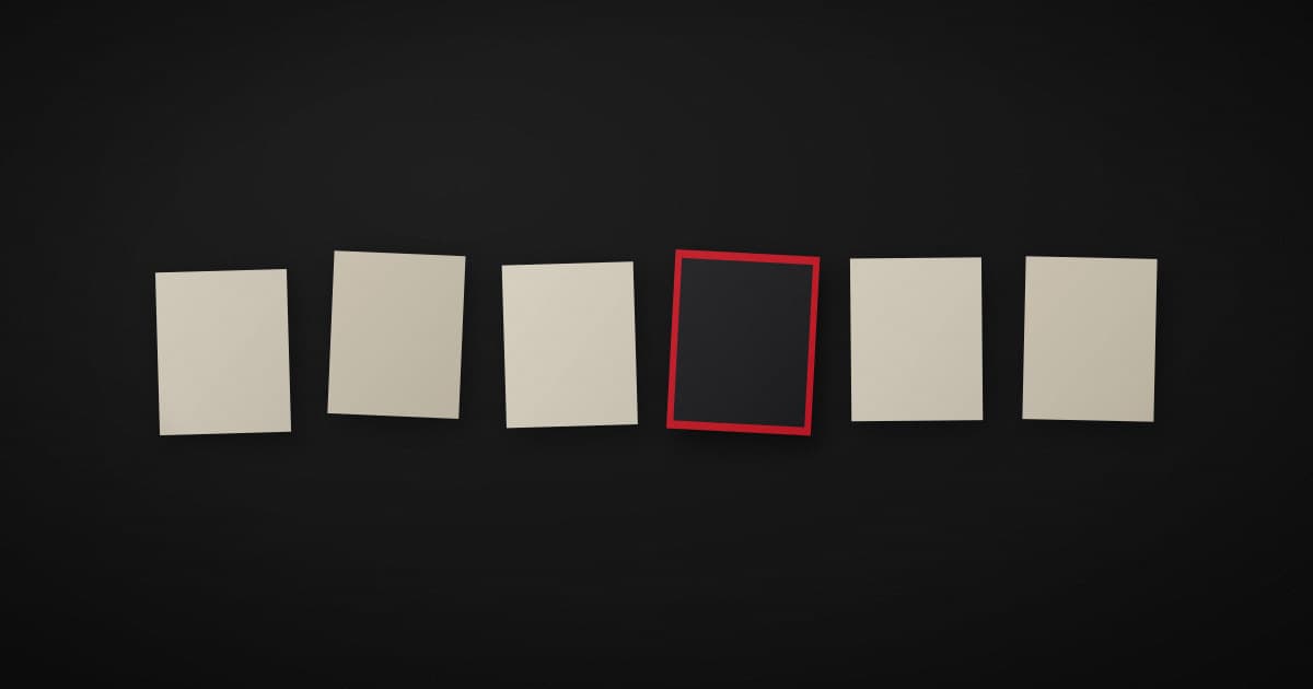 A row of pale paper cards on a dark surface, evenly spaced, with one card turned face down and edged in crimson