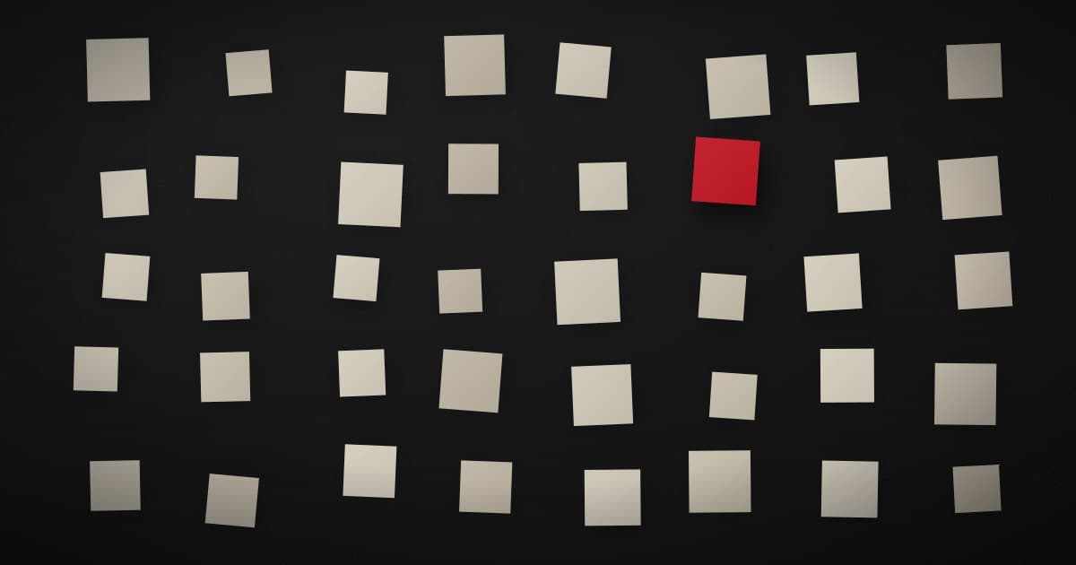 A wide scatter of pale paper squares across a dark surface with a single crimson square held apart from the rest